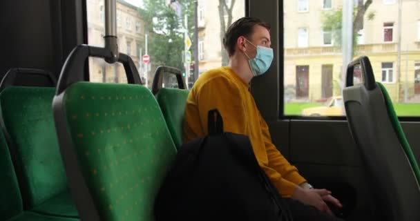 Молодий чоловік носить захисну медичну маску для захисту від вірусних захворювань, сидячи в трамваї і дивлячись крізь вікно. концепція пандемії та охорони здоров'я . — стокове відео