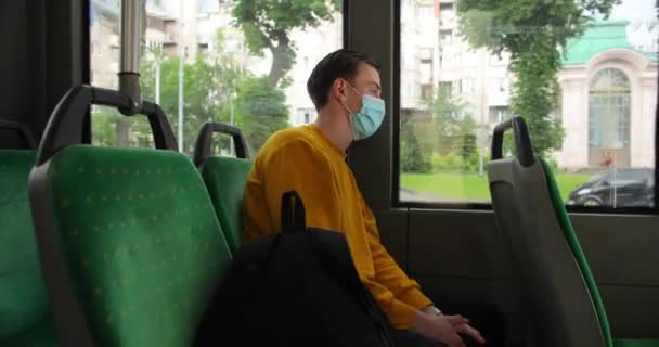 Молодий кавказький чоловік їде на автобусі з медичною маскою на обличчі. Сумний хлопець з алергією дивиться на дорогу через вікно. Захист від вірусів 4K — стокове відео