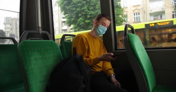 Hombre joven con teléfono inteligente que usa mascarilla médica de protección facial para la protección contra enfermedades virales sentado en el autobús. turismo, sanidad y concepto de pandemia — Vídeo de stock