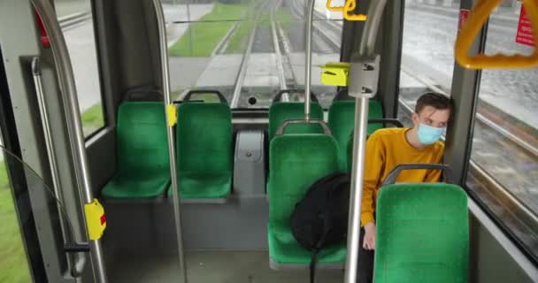 노란 스웨터를 입고 보호용 마스크를 쓰고 있는 한 청년이 빈 전차 안에 앉아 있습니다. 세계에서 유행하고 있는 코로나 바이러스 — 비디오