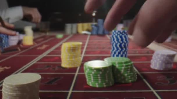 カジノにチップを置く人間の手でルーレットテーブルを閉じます。カジノのルーレットテーブルの後ろに座ってウイスキーや喫煙葉巻を飲みながら賭けをします — ストック動画