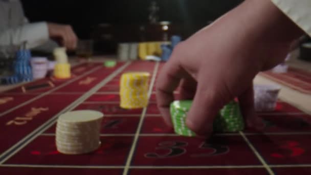 カジノにチップを置く人間の手でルーレットテーブル。認識できない人々はカジノのルーレットテーブルの後ろに座って、ウィスキーと喫煙葉巻を飲みながら賭けをします。ルーレットホイールイン — ストック動画