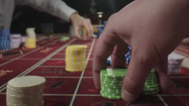 Fecha. Mesa de roleta com mãos humanas a colocar fichas no casino. Pessoas irreconhecíveis sentam-se atrás da mesa de jogo, bebendo uísque e fumando charutos enquanto fazem apostas — Vídeo de Stock