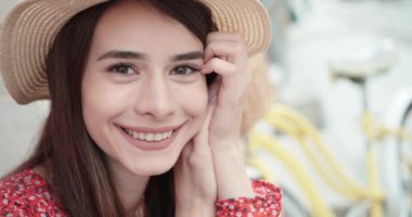 Uzun, parlak saçları olan zarif genç bir kadın mutlu bir şekilde dışarıda yürürken poz veriyor. Havalı yaz şapkalı mutlu bir kızın güneş ışığının tadını çıkarırken çekilmiş açık hava fotoğrafı..