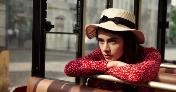 Menina atraente em um vestido vermelho e chapéu senta-se no ônibus e descansa no assento. retrato de menina triste — Vídeo de Stock