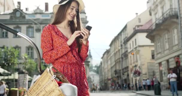 Schoonheid met vintage fiets. Mooie jonge glimlachende vrouw met smartphone staan in de buurt van haar vintage gele fiets met mand — Stockvideo