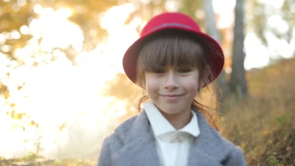Mooi glimlachend meisje met lang brunette haar in grijze jas met rode hoed die bij zonsopgang in het bos verblijft. Mistige herfst landschap van het platteland. 4K-video. — Stockvideo