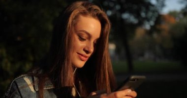Çekici kız gün batımında parkta telefon kullanıyor..