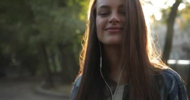 Çekici kız parkta müzik dinler dans eder ve gülümser, güzel güneş ışığı saçlarında parlar..