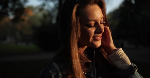 Çekici kız mutlulukla kulaklıkla müzik dinliyor. Parktaki telefondan.. — Stok video