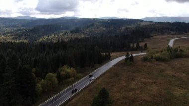 Sonbahar sezonunda gün batımında dağ virajlı bir hava aracı videosu. Yolda iki araba.