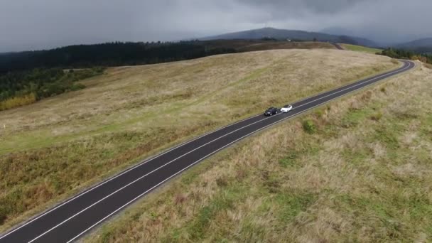 Twee auto 's halen elkaar in. autoracen. auto 's rijden op een mooie vlakke weg in een veld op een achtergrond van bossen en bergen — Stockvideo