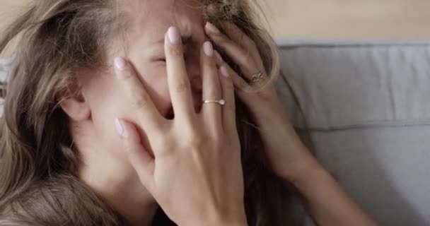 Une femme triste assise sur le canapé et tenant sa tête dans ses mains. Triste jeune femme pleure avec la paume à la face. — Video