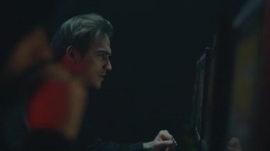 Kapüşonlu genç adam karanlık odada bilgisayar oyunları oynuyor. Oyun bağımlılığı. Bir bilgisayar kulübünde kumar oynayan genç bir adam. Çevrimiçi kumarhane.