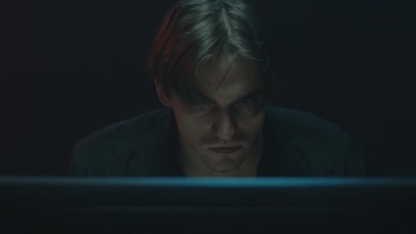 Zaniepokojony młody człowiek siedzi przed monitorem za ciemnym tłem pokoju. — Wideo stockowe