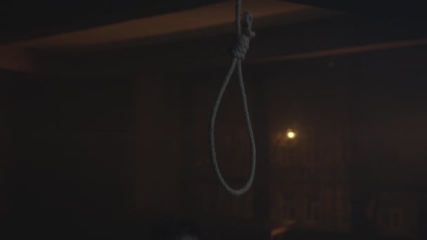 En man trycker huvudet i en snara för att begå självmord. hängning. ledsen man håller en snara i ett mörkt rum mot fönstret, beslutar sig för att begå självmord. — Stockvideo