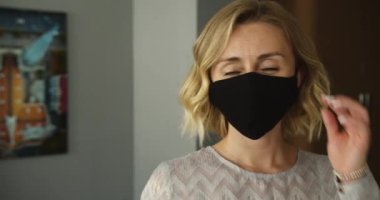Tıbbi maskesini çıkaran kadın. Portreyi yakından çek. Genç mutlu sarışın kadın koruyucu tıbbi maskeyi içeride çıkarıyor. Salgın Covid-19.