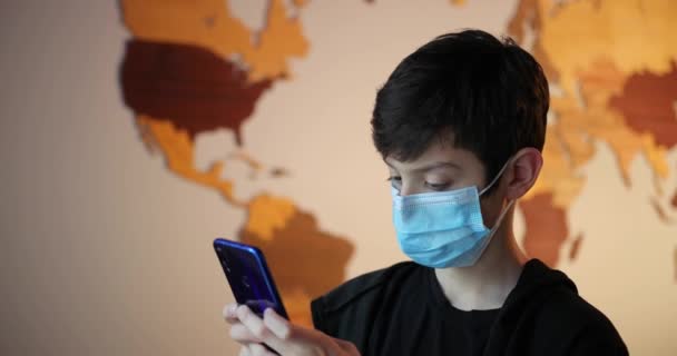 Tonårspojke, ett barn i medicinsk mask. Begreppet epidemi, influensa, skydd mot sjukdomar, vaccinering. Sjuk pojke i mask använder en smartphone — Stockvideo