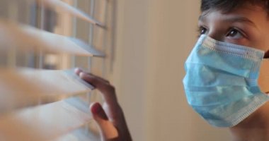 Kendini izole eden küçük çocuk pencereden dışarı bakıyor. Covid-19 kendini izole ediyor. Gönüllü kendini izole etme kavramı. Çocuk salgın sırasında pencereden bakıyor.