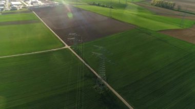 Boş yeşil ve gri alanlar arasında gökyüzüne karşı elektrik desteklerinin drone görüntüsü. Medeniyet arka planda görülebilir. Güneşli bir gün, yaz, kırsal, yüksek voltaj hattı. 4K video.