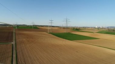 Gökyüzüne karşı boş yeşil ve sarı alanlar arasında elektrik desteklerini gösteren videoyu kapat. Medeniyet arka planda görülebilir. Güneşli bir gün, yaz, kırsal, yüksek voltaj hattı. 4K video.