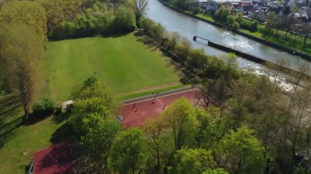 Vista aérea de la cancha de baloncesto y fútbol donde los adolescentes están jugando al fútbol. Drone está girando alrededor de la corte y dispara áreas verdes, río y la ciudad de Weinsburg alrededor. Vídeo 4K. — Vídeo de stock