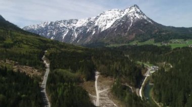 Avustralya köyünün havadan görünüşü ve baharda Alpler 'in karlı zirveleri. Yeşil orman, tarla, beyaz gökyüzü ve güneşli gün. Avrupa. High Mountain Range 'den panoramik manzara. 4K video.