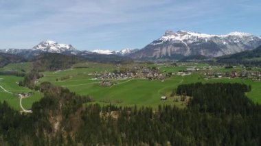 Avustralya köyünün insansız hava aracı manzarası ve baharda Alplerin karlı zirveleri. Yeşil orman, tarla, beyaz gökyüzü ve güneşli gün. Avrupa. High Mountain Range 'den panoramik manzara. 4K video.