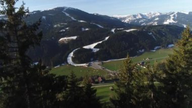 Avustralya köyünün insansız hava aracı manzarası ve baharda Alplerin karlı zirveleri. Yeşil orman, tarla, beyaz gökyüzü ve güneşli gün. Avrupa. High Mountain Range 'den panoramik manzara. 4K video.