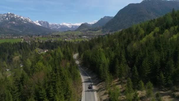 Svart bil kör genom skogen till den austriska byn mitt i de österrikiska alperna på våren. Landskap av austriska byn och lättskötta snötäckta berg. 4K-video. — Stockvideo