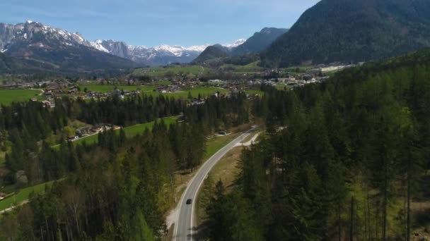 Schwarzes Auto, das im Frühling durch den Wald in das österreichische Dorf mitten in den österreichischen Alpen fährt. Landschaft des österreichischen Dorfes und leicht schneebedeckte Berge. 4K-Video. — Stockvideo