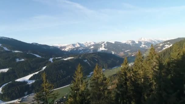Vue panoramique du village autrichien et des sommets enneigés des Alpes au printemps. Forêt verte, champ, ciel blanc et journée ensoleillée. L'Europe. Vue panoramique depuis la haute montagne. Vidéo 4K. — Video