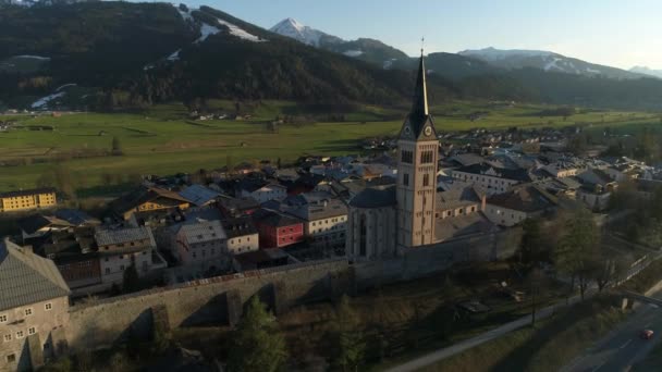 Panoramic view of beautiful landscape of small spring town among Austrian alpine mountains. Drone video of church and small houses on the background of mountains easily covered with snow. 4K video. — Stock Video