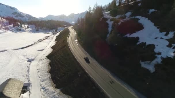 Svart bil rider på en motorväg bland de alpina bergen täckt med snö. Video av den austriska byn mitt i de österrikiska alperna på våren. 4K-video. — Stockvideo