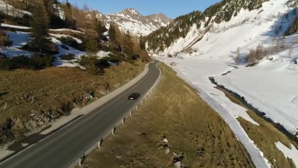 Svart bil rider på en motorväg bland de alpina bergen täckt med snö. Video av den austriska byn mitt i de österrikiska alperna på våren. 4K-video. — Stockvideo