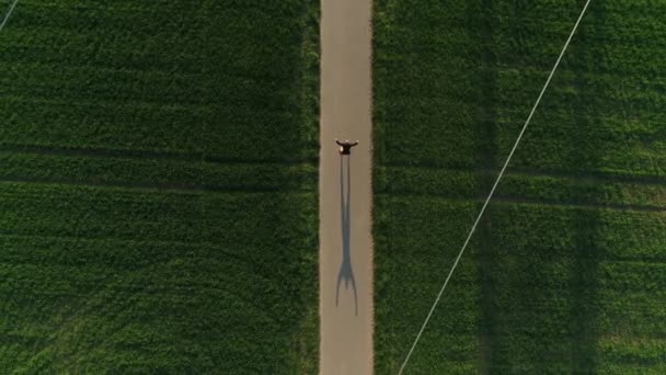 Молодой лысый человек кричит в полную силу, оставаясь на пустом асфальтовом шоссе между зелеными полями сельхозугодий на закате. Вид с воздуха. 4K видео. — стоковое видео