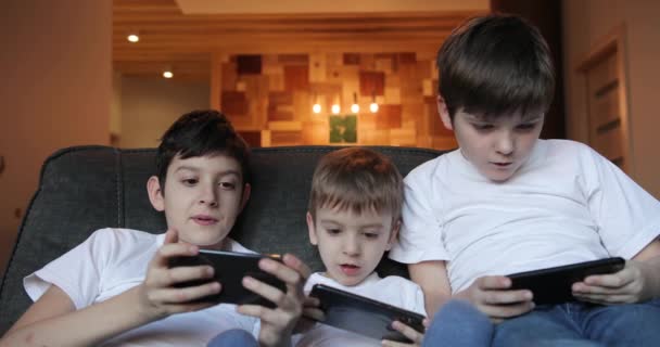 Inomhusporträtt av tre pojkbarn som leker med telefoner. söta barn spelar spel på smartphone i hemmet — Stockvideo
