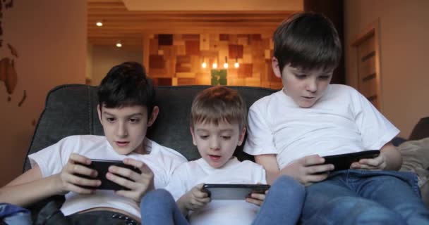 Niños jugando en un smartphone en casa en el sofá. generación de teléfonos inteligentes. Uso excesivo del teléfono celular — Vídeo de stock