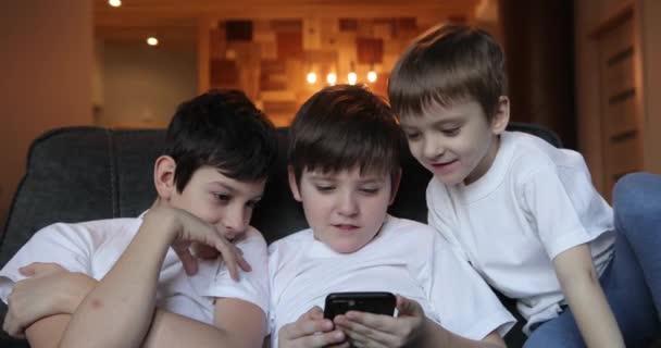 Lachende kinderen die grappige video keken op een smartphone die samen op de bank zat. kinderen die graag spelletjes spelen of zich vermaken met mobiele apps op de telefoon thuis. — Stockvideo