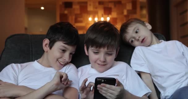 Három kis mosolygós fiú testvérek játék vagy szörfözés interneten okostelefonok — Stock videók