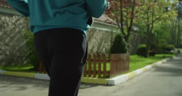 Вид сзади. спортивная ходьба. мужчина в брюках и синей толстовке, идущий по дороге. — стоковое видео