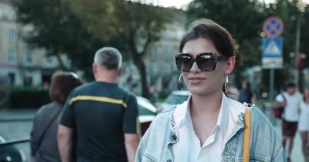Güneş gözlüklü ve büyük yuvarlak küpeli genç bir kadın sokakta yürüyor ve gülümsüyor.. — Stok video