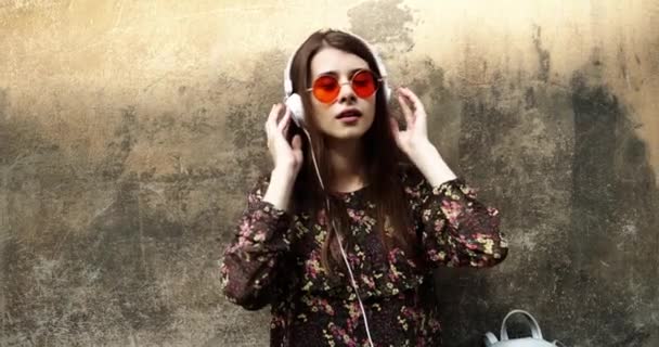 Jovencita hipster posando en la calle escuchando música y dansing, retrato de moda al aire libre, auriculares reproductor de mp3, gafas de sol, estilo calle, labios rojos componen, cabello, bronceado, lindo, celebridades — Vídeos de Stock