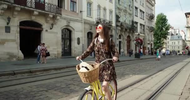 Aantrekkelijk meisje met lang haar rijdt door de straat op een gele retro fiets tegen de achtergrond van de oude stad — Stockvideo