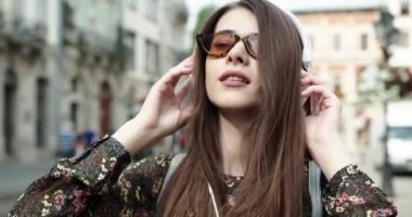 Mutlu bir kızın portresi, güneşli bir yaz gününde, sokakta bulunan akıllı bir telefondan kablosuz kulaklıkla müzik dinliyor..