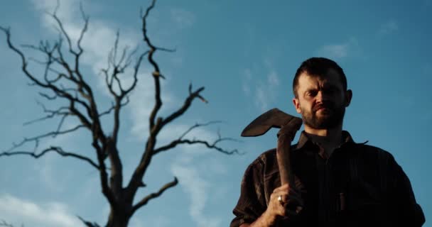 Bottom view. lumberjack with a beard stands near a dry tall tree with an ax on his shoulder — Stock Video