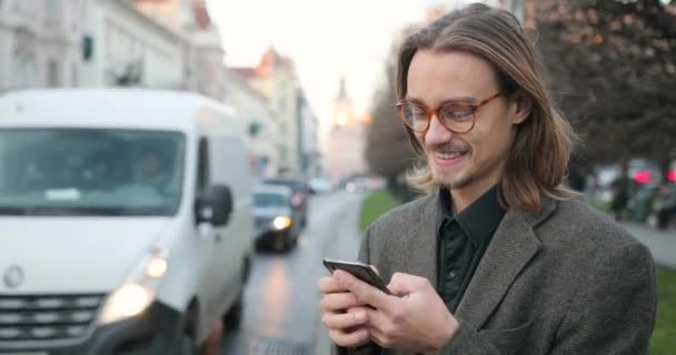 Sakallı çekici genç adam akıllı telefondan mesaj yazıyor. Adamın çok iyi bir ruh hali var. Akıllı telefon kullanan gülümseyen genç adam. Genç adam mutlu görünüyor. — Stok video