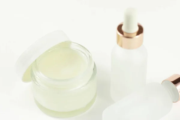 Yüz kremi ve pipetli şeffaf şişeler olan cam kozmetik kabı, beyaz arka planda cilt bakım laboratuvarı, kozmetik ilaç kavanozu.