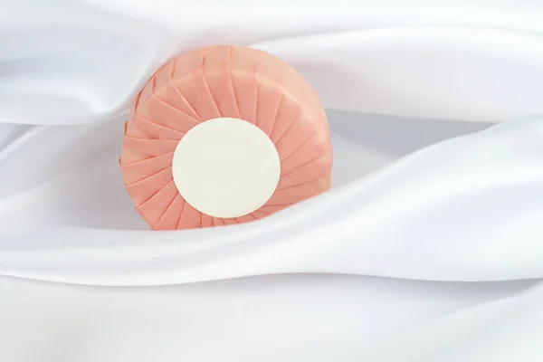白色丝绸背景粉红纸包中圆形固体肥皂条 — 图库照片