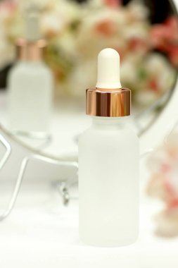 Beyaz çiçekli pipetli mat beyaz kozmetik şişesi ve ayna yansıması, cilt bakımı, kaplıca güzellik terapisi.